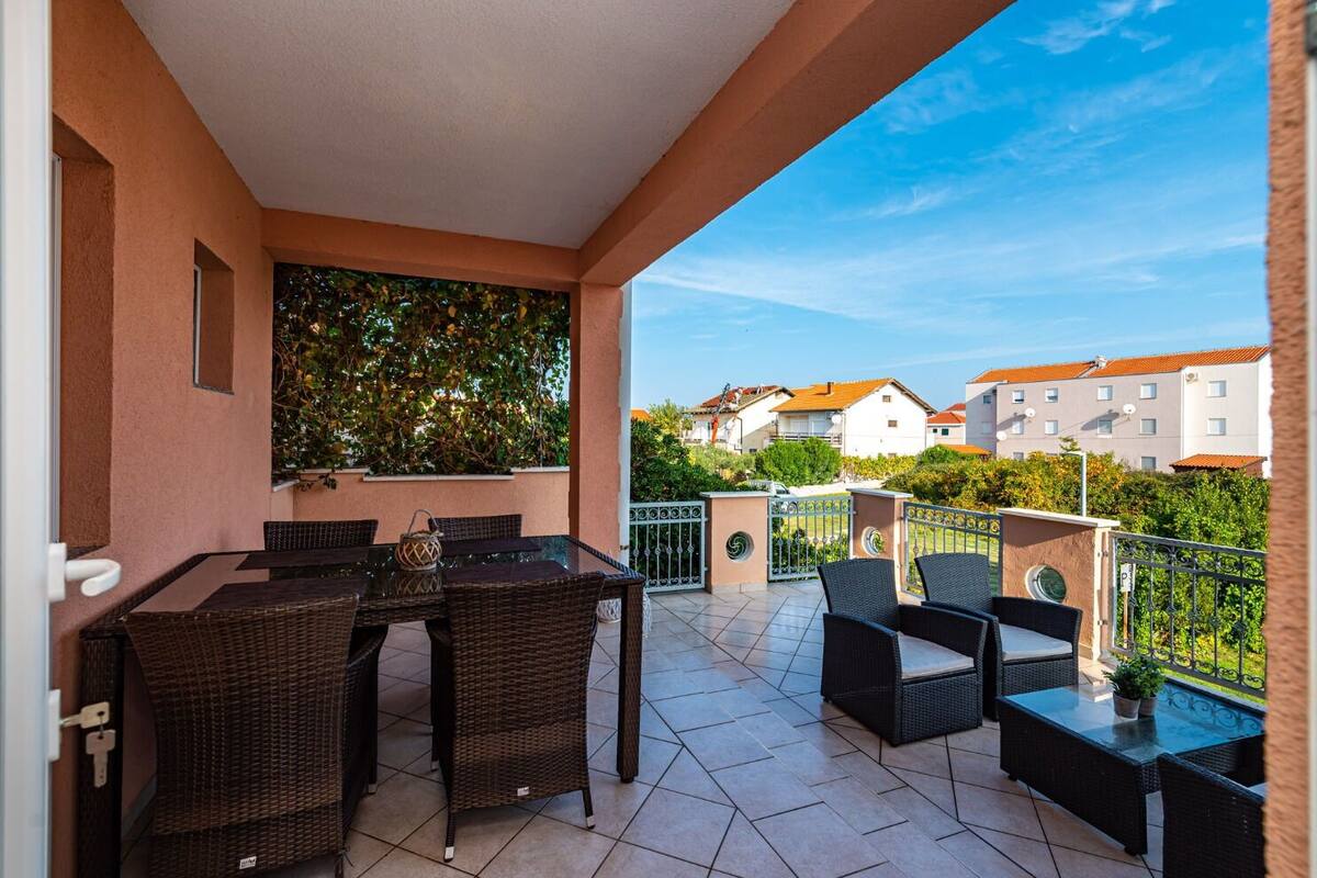 Un balcone con tavolo e sedie, vista su case e un muro verde.