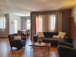 A living room with a sofa, armchairs, and a coffee table. There is a dining area in the background with a table and chairs. - Apartments Nada (Novalja)
