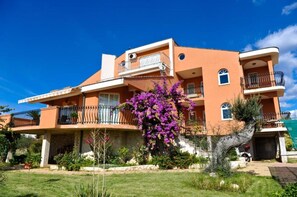 A two-story building with balconies, a garden with purple flowers, and a clear blue sky. - Apartments Nada (Novalja)