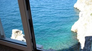 A coastal view through a window with a clear blue sea and rocky cliffs. - House Bernardica (Vrbnik)