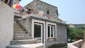 A stone building with a small window and a door, a set of concrete stairs leading up to it, and a colorful umbrella in the background. - House Bernardica (Vrbnik)