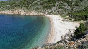A coastal landscape with a sandy beach, clear blue waters, and rocky terrain with sparse vegetation. - House Bernardica (Vrbnik)
