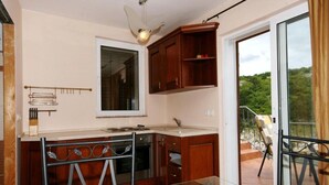 A modern kitchen with wooden cabinets, a glass table, and a view of greenery outside. - House Bernardica (Vrbnik)