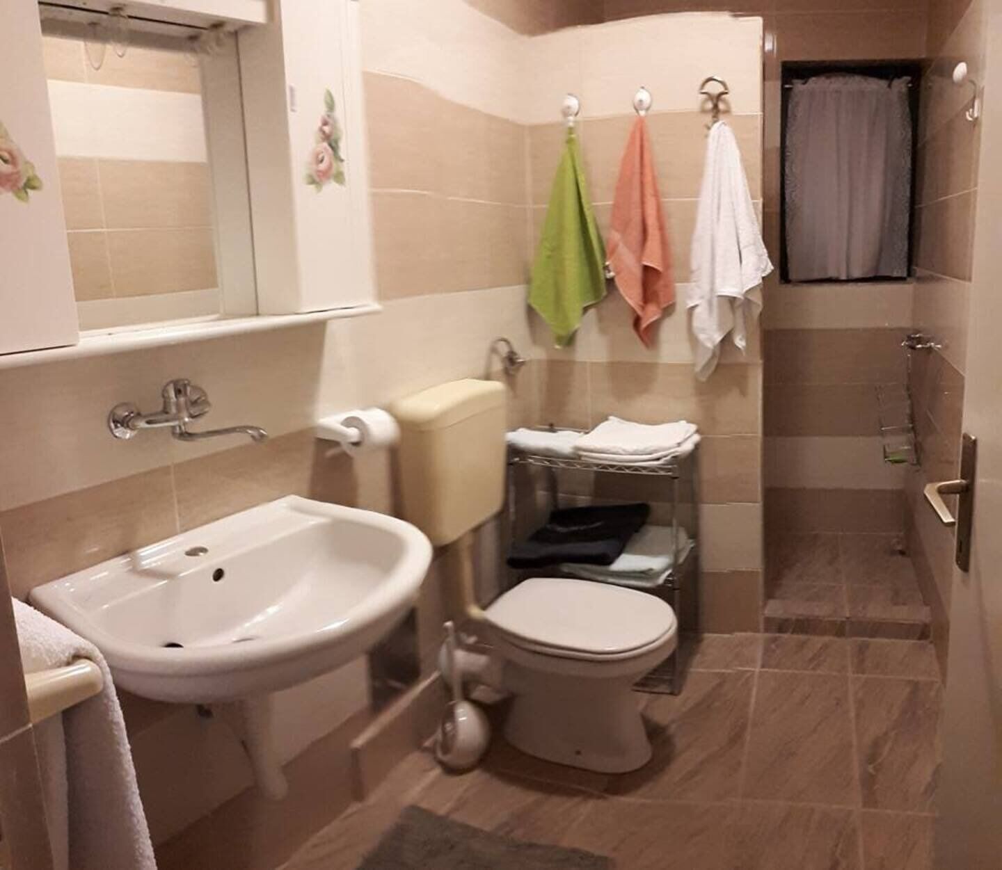 Ein Badezimmer mit Waschbecken, Toilette und Dusche. Handtücher hängen an der Wand, und es ist ein Toilettenpapierhalter vorhanden.