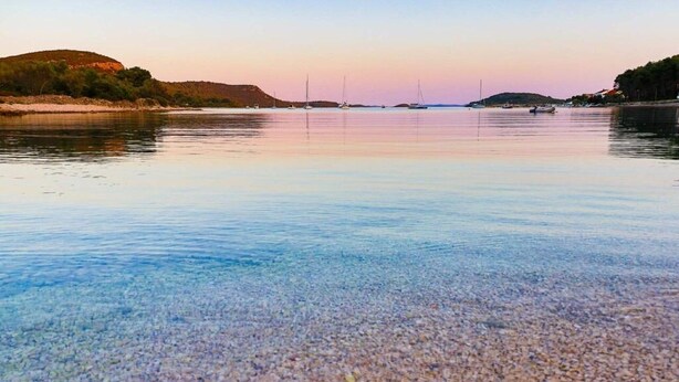 A calm lake with clear water, boats, and a hilly landscape in the background. - Apartments Novis (Kali)