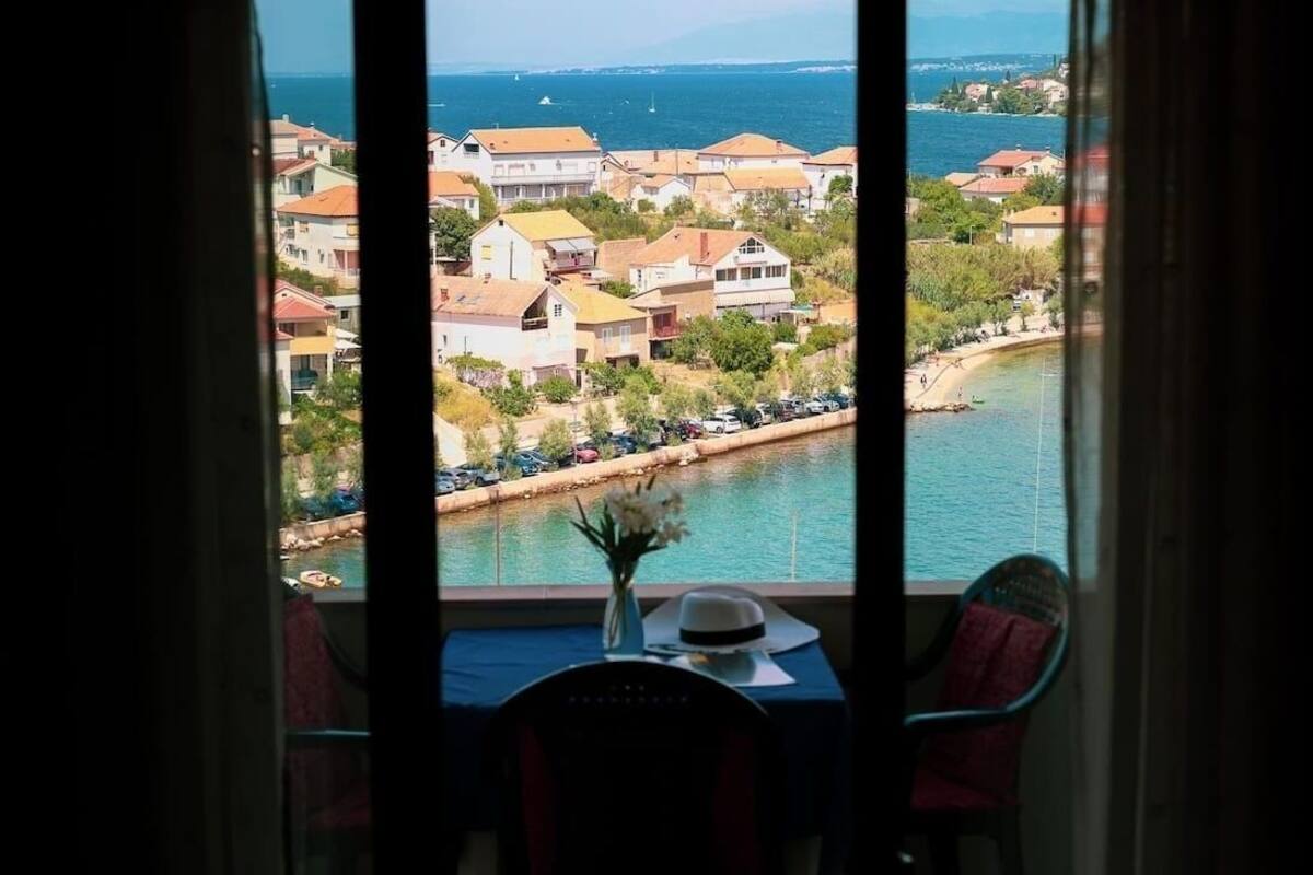A view from a window overlooking a coastal town with buildings and a body of water.