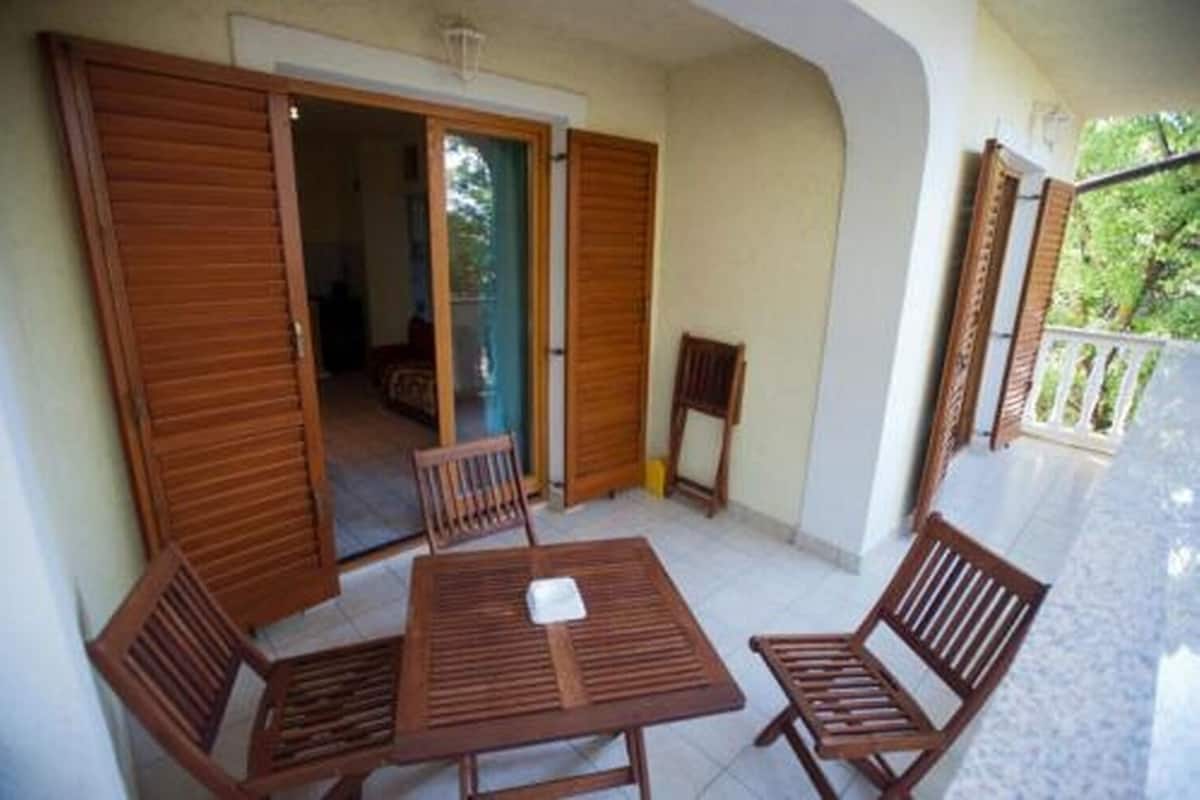 Un balcón con mobiliario de madera, incluyendo una mesa y sillas, y una puerta corrediza que da a un espacio interior.