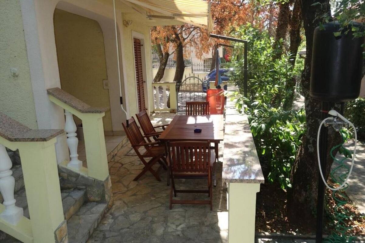 Un patio con una mesa y sillas de madera, suelo de piedra y una escalera que sube a un nivel superior.