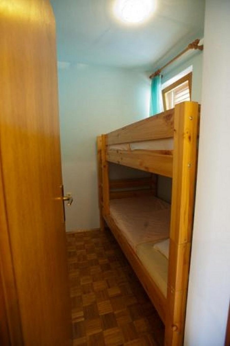Pieni, kapea huone, jossa on kerrossänky ja puuovi.