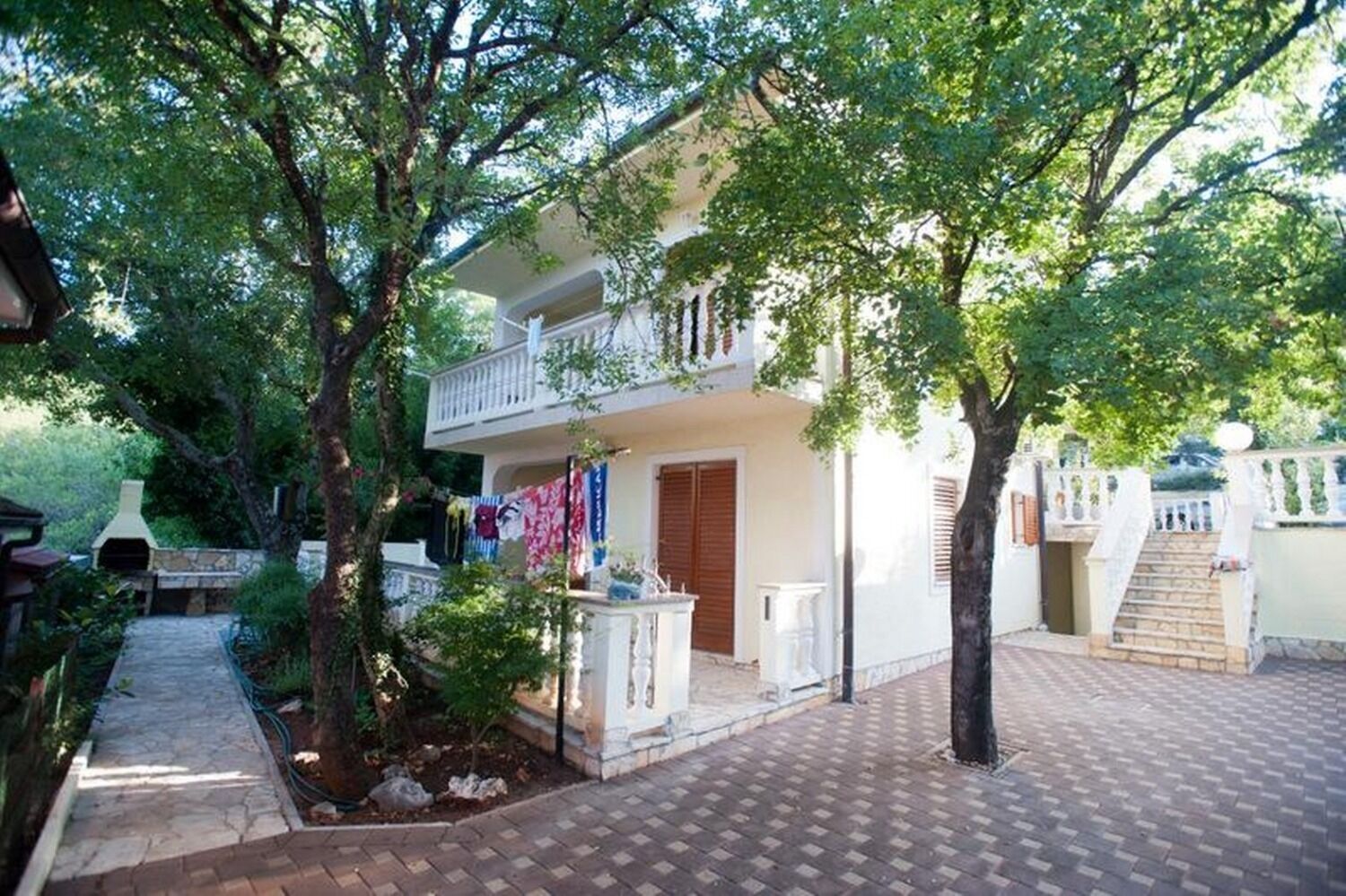 A two-story building with a balcony, surrounded by trees and a paved walkway.