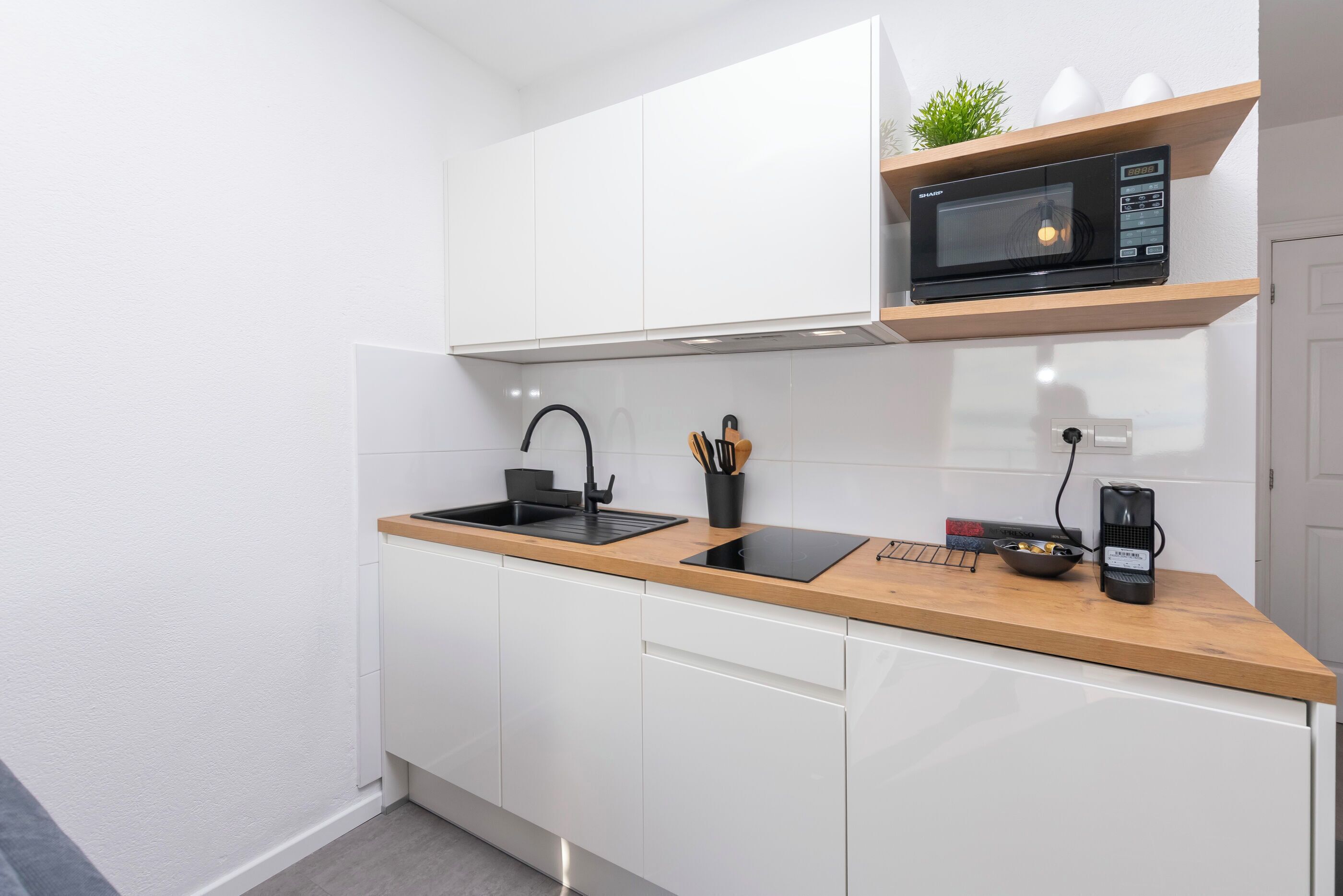 A modern kitchen with white cabinets, a wooden countertop, a built-in microwave, and a coffee maker.