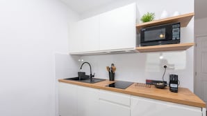 Cozinha moderna com armários brancos, bancada de madeira, micro-ondas embutido e máquina de café.