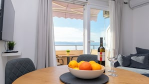 Uma área de refeições com uma mesa, uma tigela de frutas, uma garrafa de vinho e um copo.