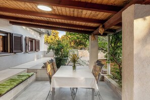 An outdoor patio with a table and chairs, a green cushioned bench, and a potted plant. - Apartment Uga (Kolan)