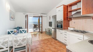 Uma cozinha compacta com armários brancos, fogão a gás e área de refeições com mesa e cadeiras.