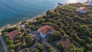 Vista aérea de uma propriedade costeira com vários edifícios, praia e vegetação densa.