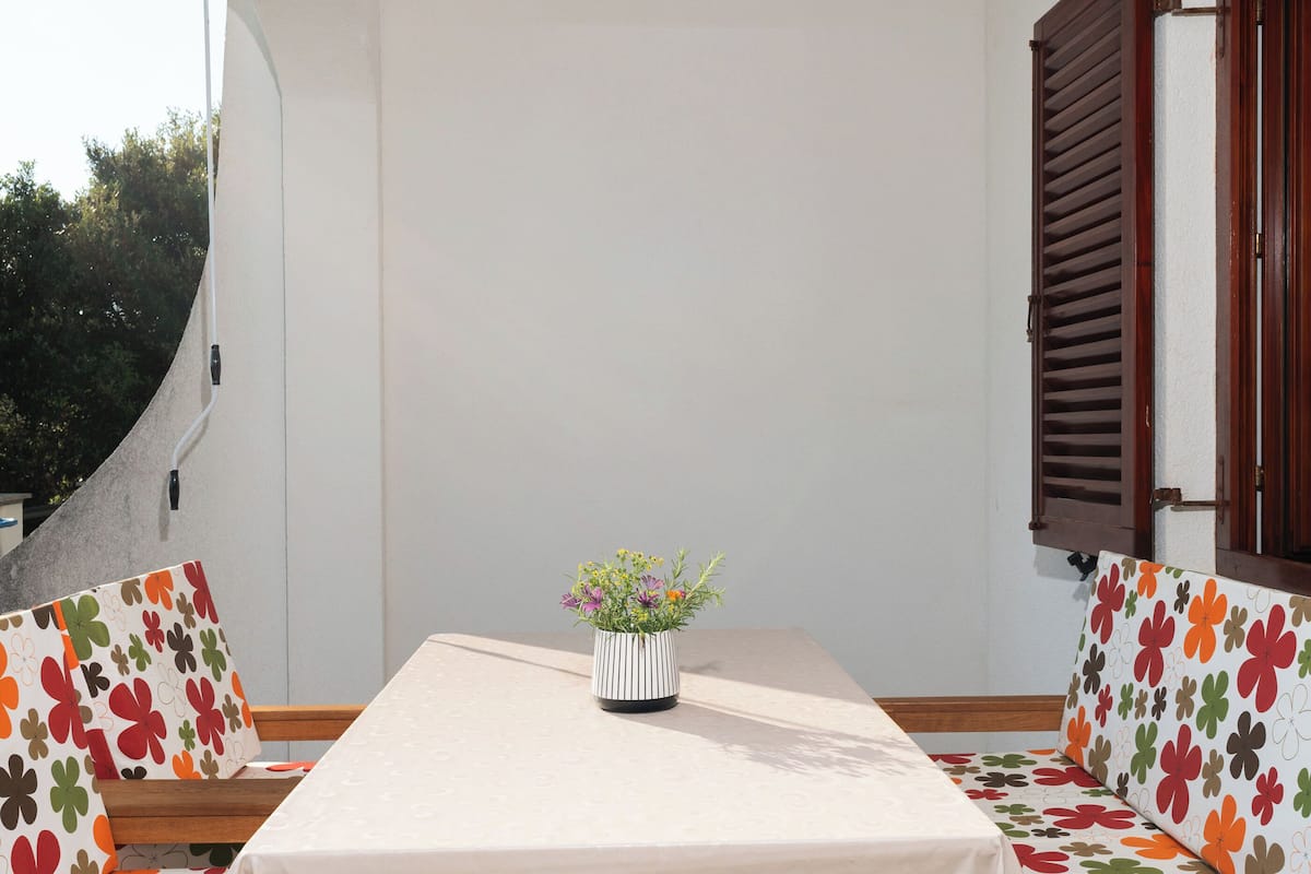 Une table recouverte d’une nappe blanche, un vase à rayures orné de fleurs et des coussins à motifs floraux.