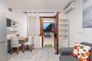 A compact living space with a dining area, a sofa, and a view through an open door to an outdoor patio. - Apartment Uga (Kolan)