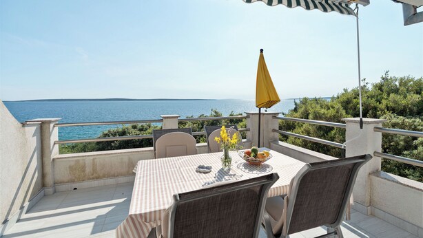 Uma varanda com mesa, cadeiras e um guarda-sol amarelo, com vista para o mar.