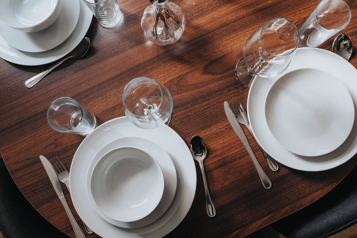 Een net gedekte eettafel met witte borden, bestek en heldere glazen.
