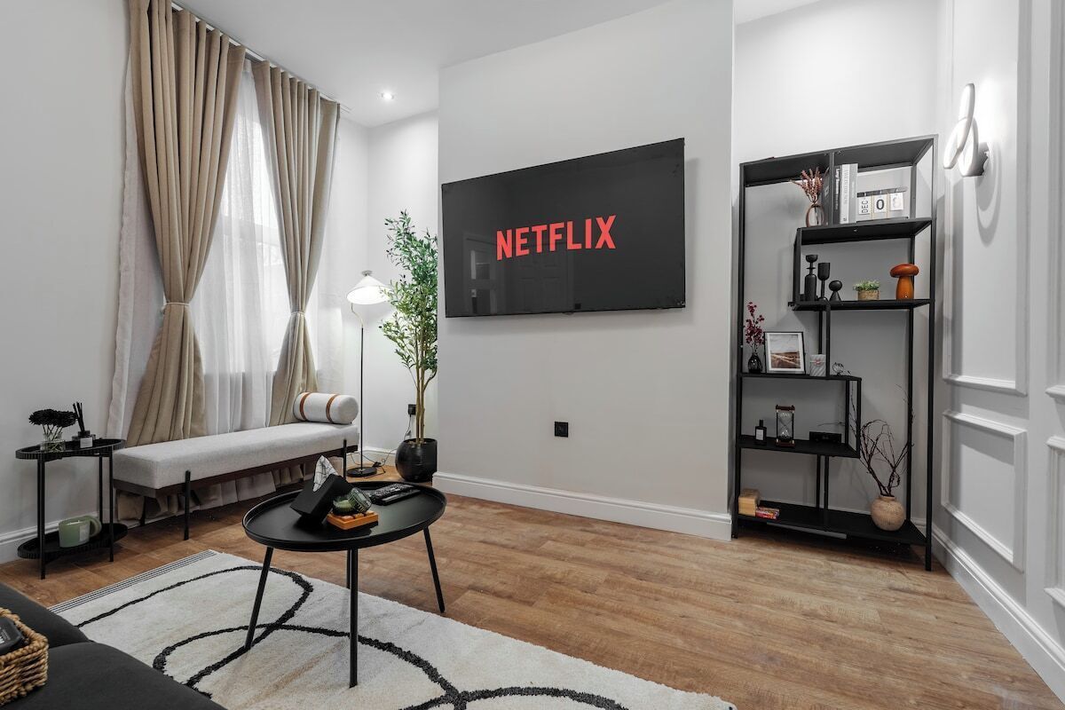 Un salon moderne avec un canapé, une table basse, un téléviseur fixé au mur et une bibliothèque.