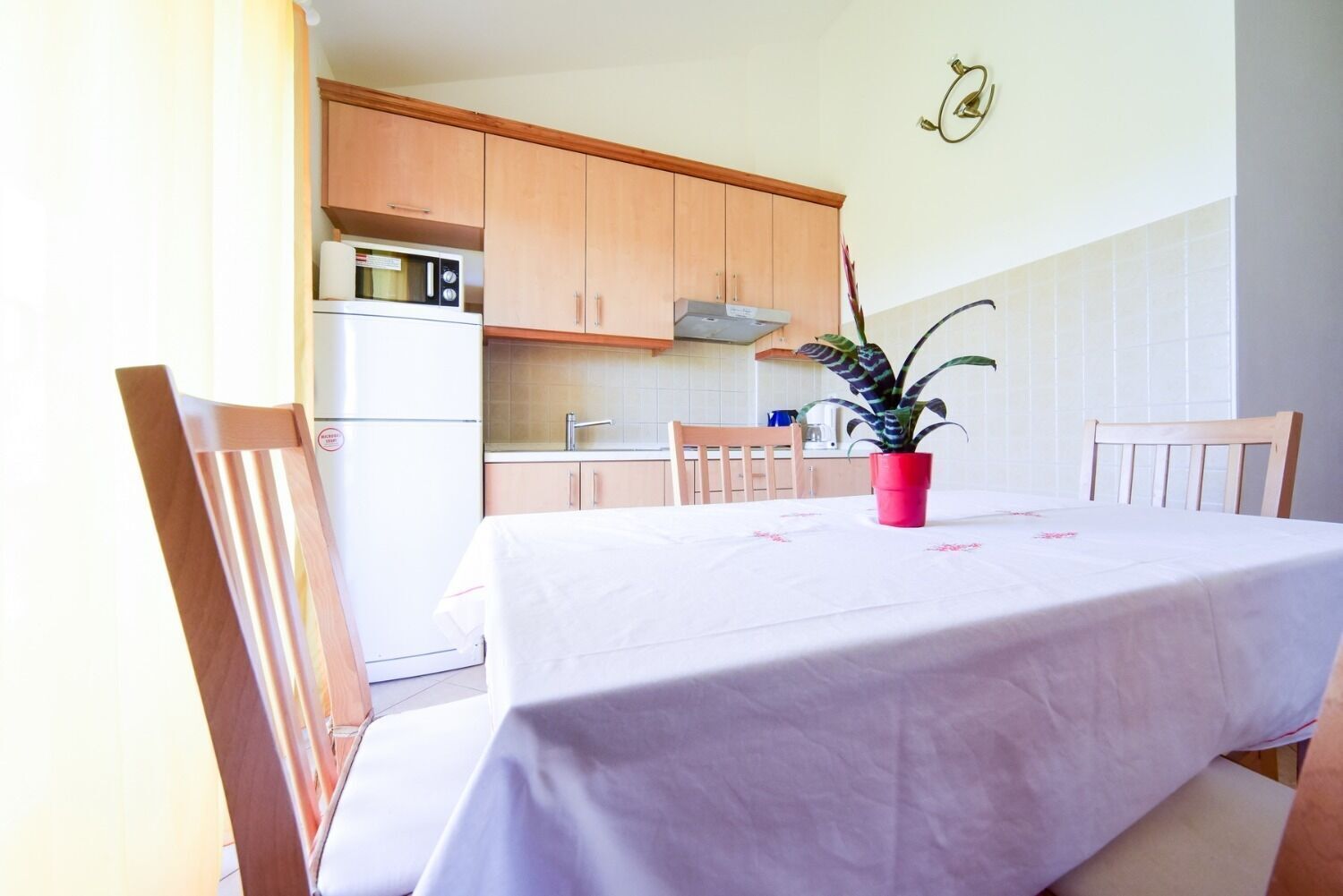 Ein Essbereich mit Tisch für zwei Personen, Holzstühlen, einem Blumentopf und einer Küche im Hintergrund.