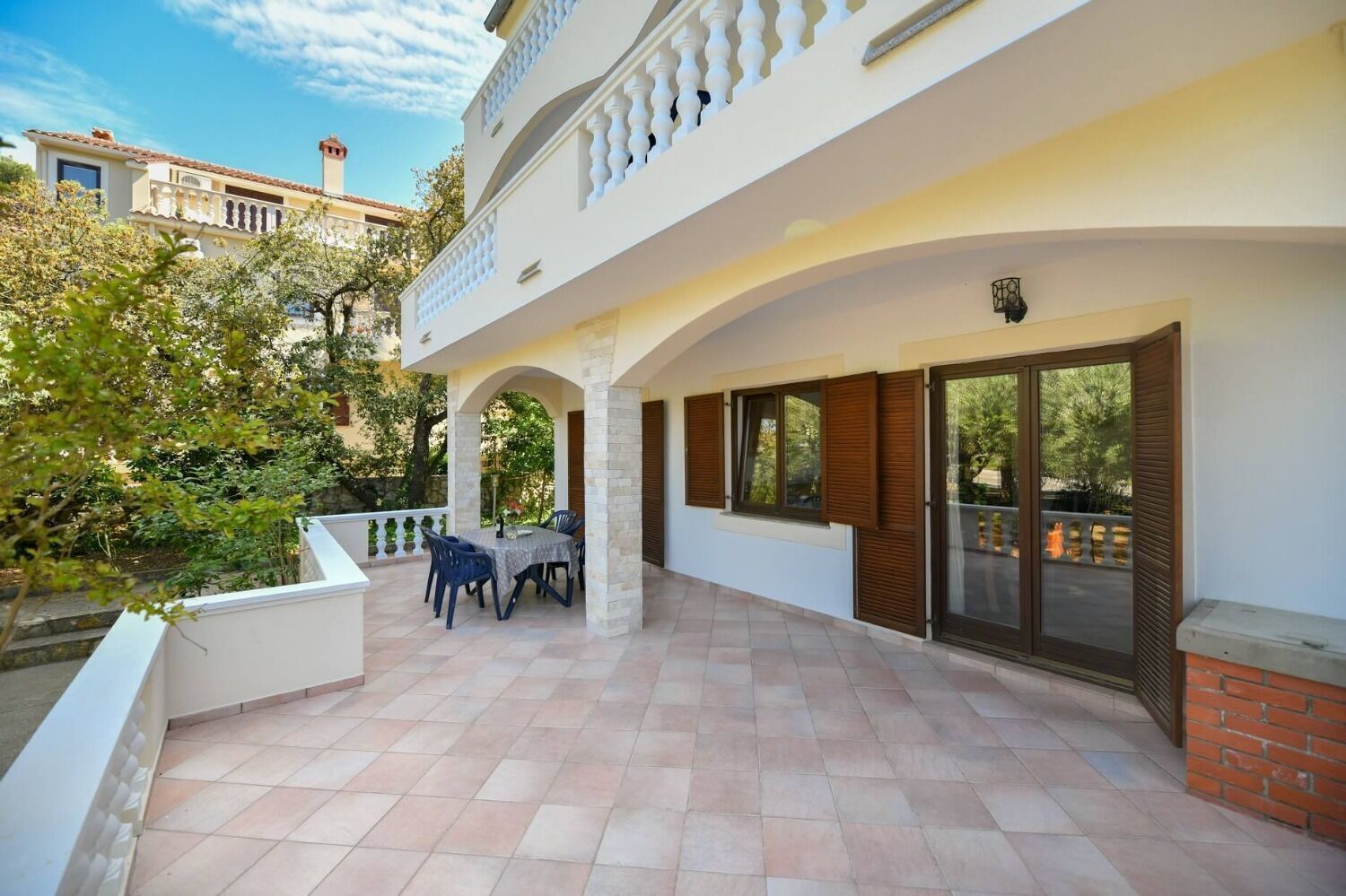 A covered outdoor patio with a table and chairs, surrounded by a white building with a balcony.