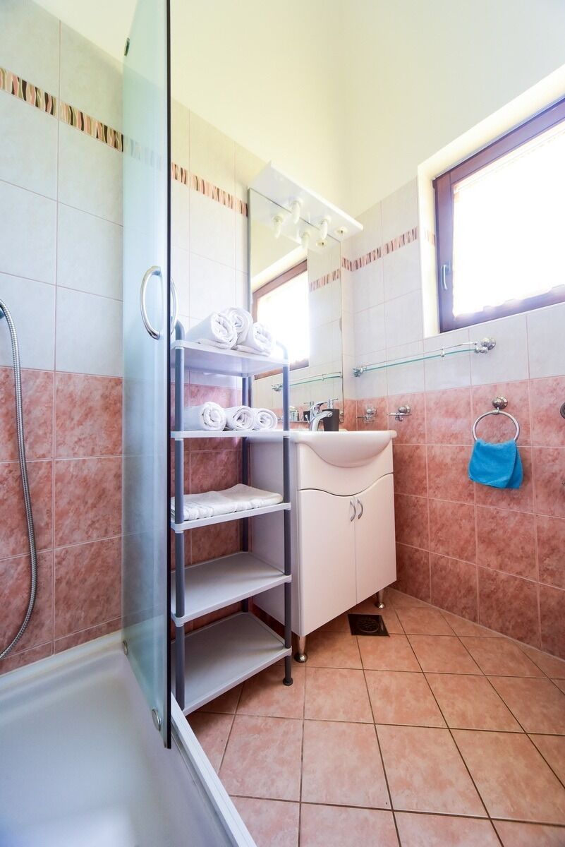 A bathroom with a glass shower enclosure, a white sink with a mirror above it, and a blue towel hanging on the wall.
