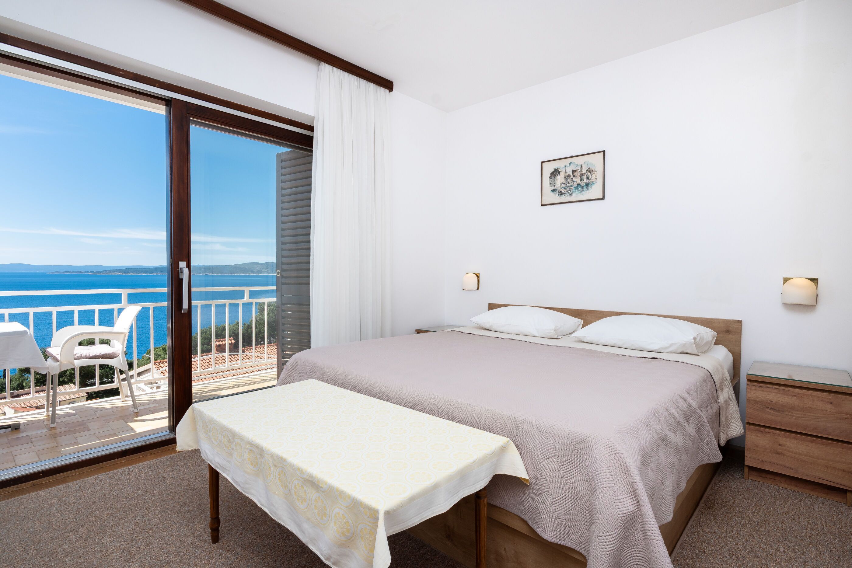 Quarto com cama, mesa de cabeceira e vista para o mar.