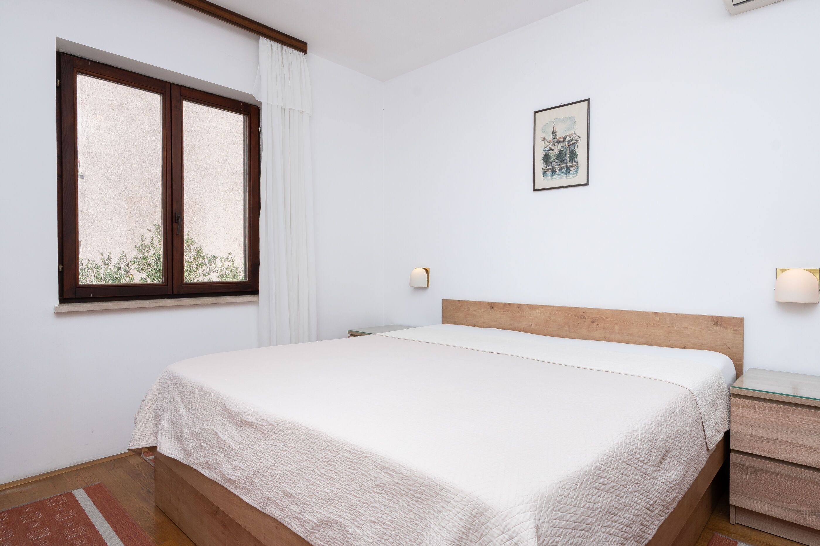 Une chambre à coucher comprenant un lit, une fenêtre, une table de chevet et une lampe fixée au mur.