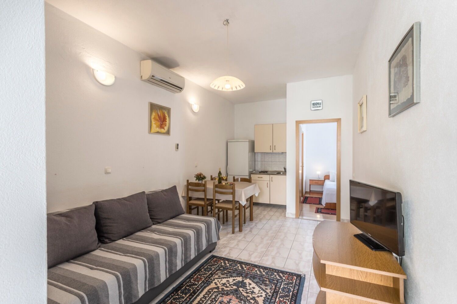 Ett kompakt bostadsutrymme med en soffa, ett matbord, en TV och ett köksområde.