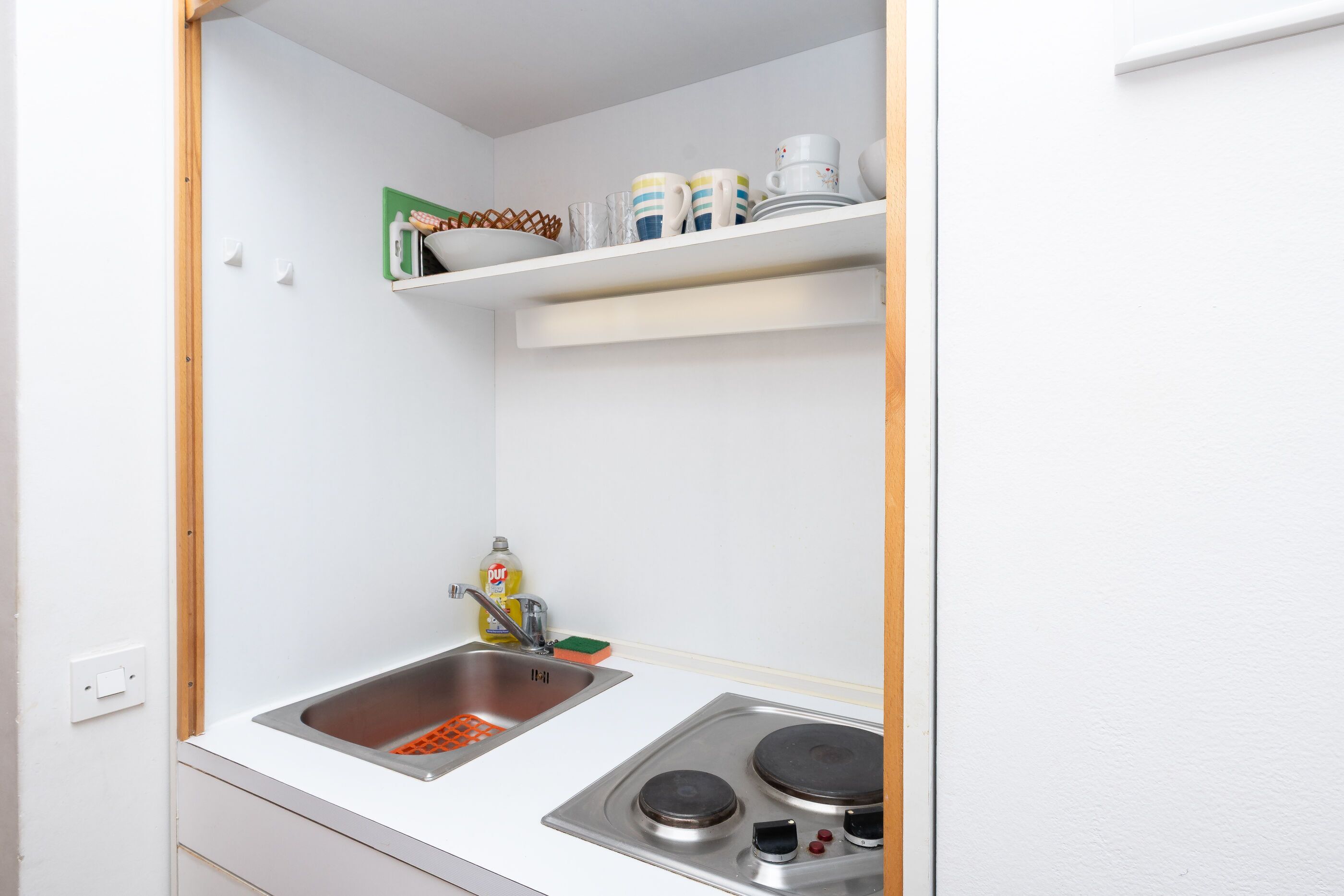 A small kitchenette with a sink, stove, and shelves above the counter.