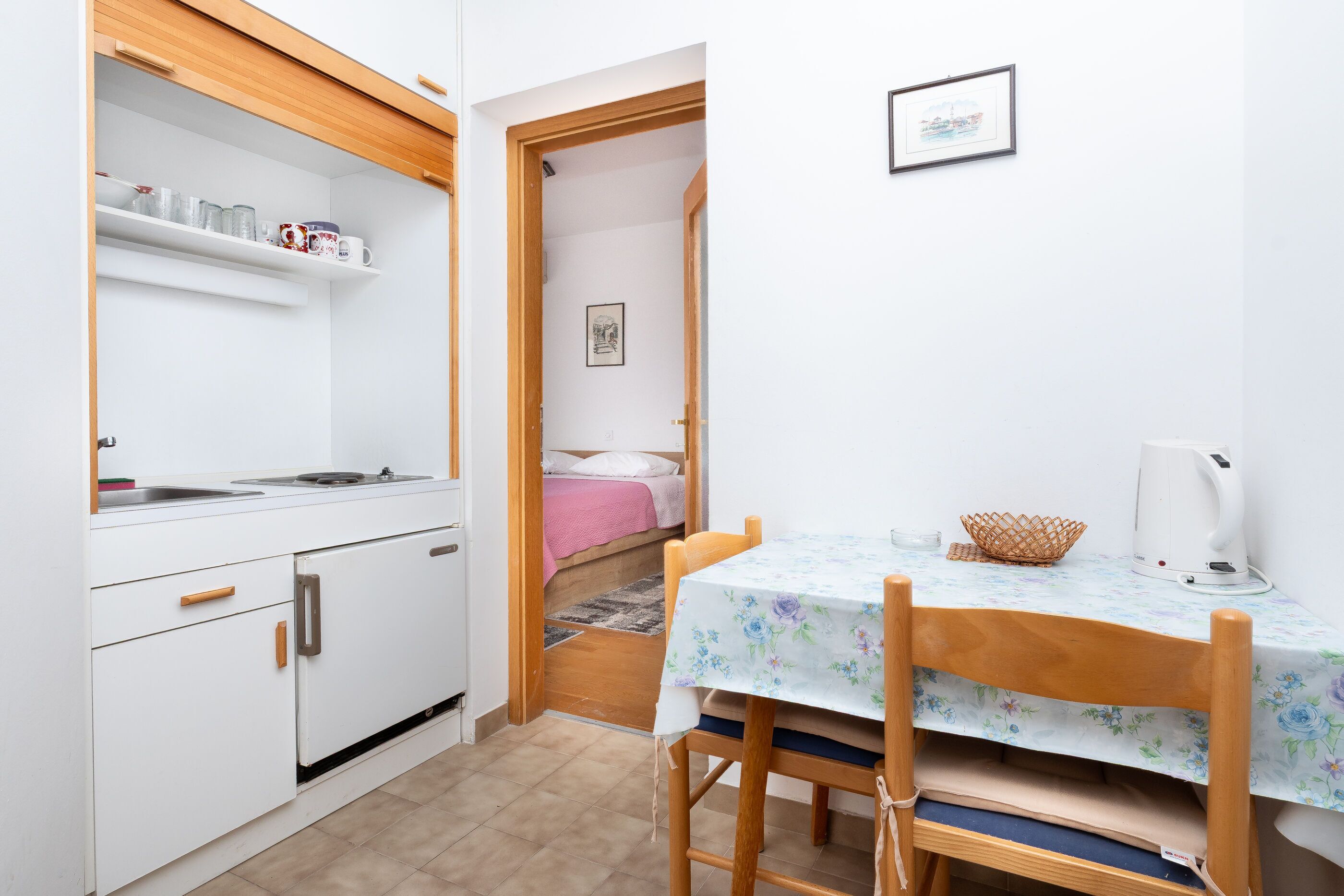 Een kleine keuken met een eettafel, een bed en een klein plankje met keukengerei.