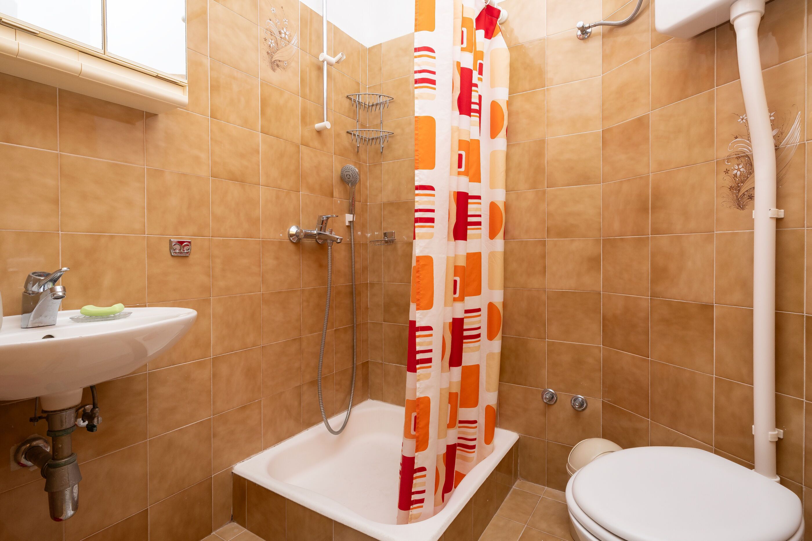 Ein Badezimmer mit Dusche, Toilette, Waschbecken und einer Duschvorhang mit geometrischem Muster.
