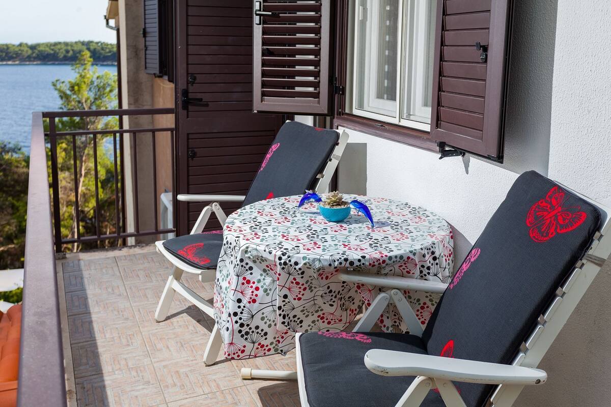 Un balcone con tavolo e due sedie, una pianta in vaso e vista sul mare.