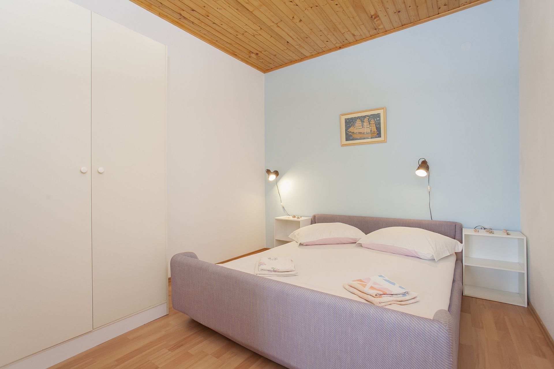 Un dormitorio con cama, mesitas de noche, armario y techo con vigas de madera.