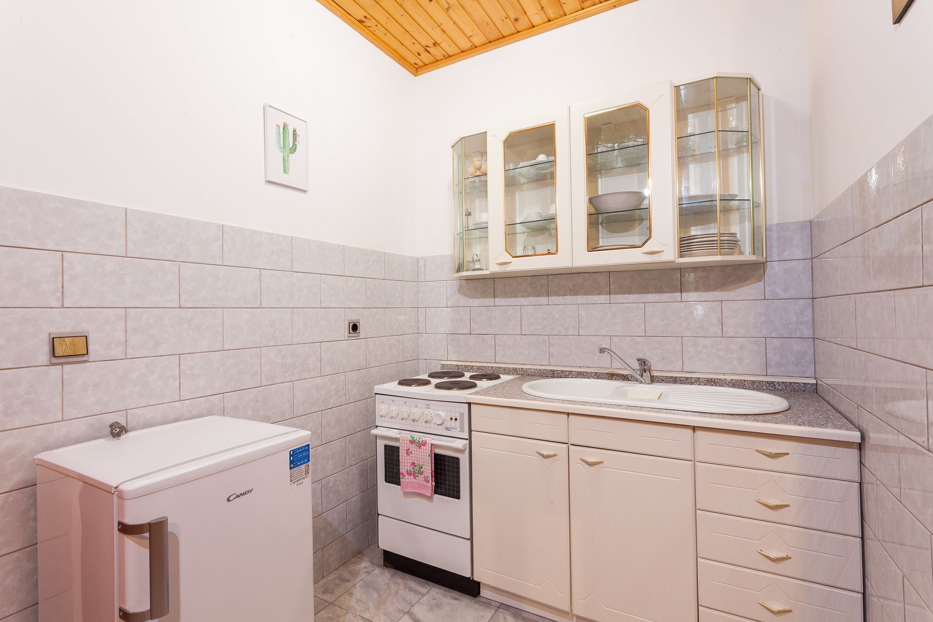 A compact kitchen with a white refrigerator, a stove, a sink, and a cabinet with glass doors.