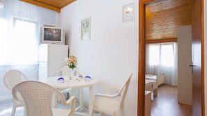 Una stanza con soffitto in legno, un tavolo bianco con sedie, una televisione e un frigorifero.