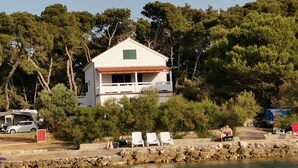 Uma casa à beira-mar com varanda, rodeada por árvores e um muro de pedra.