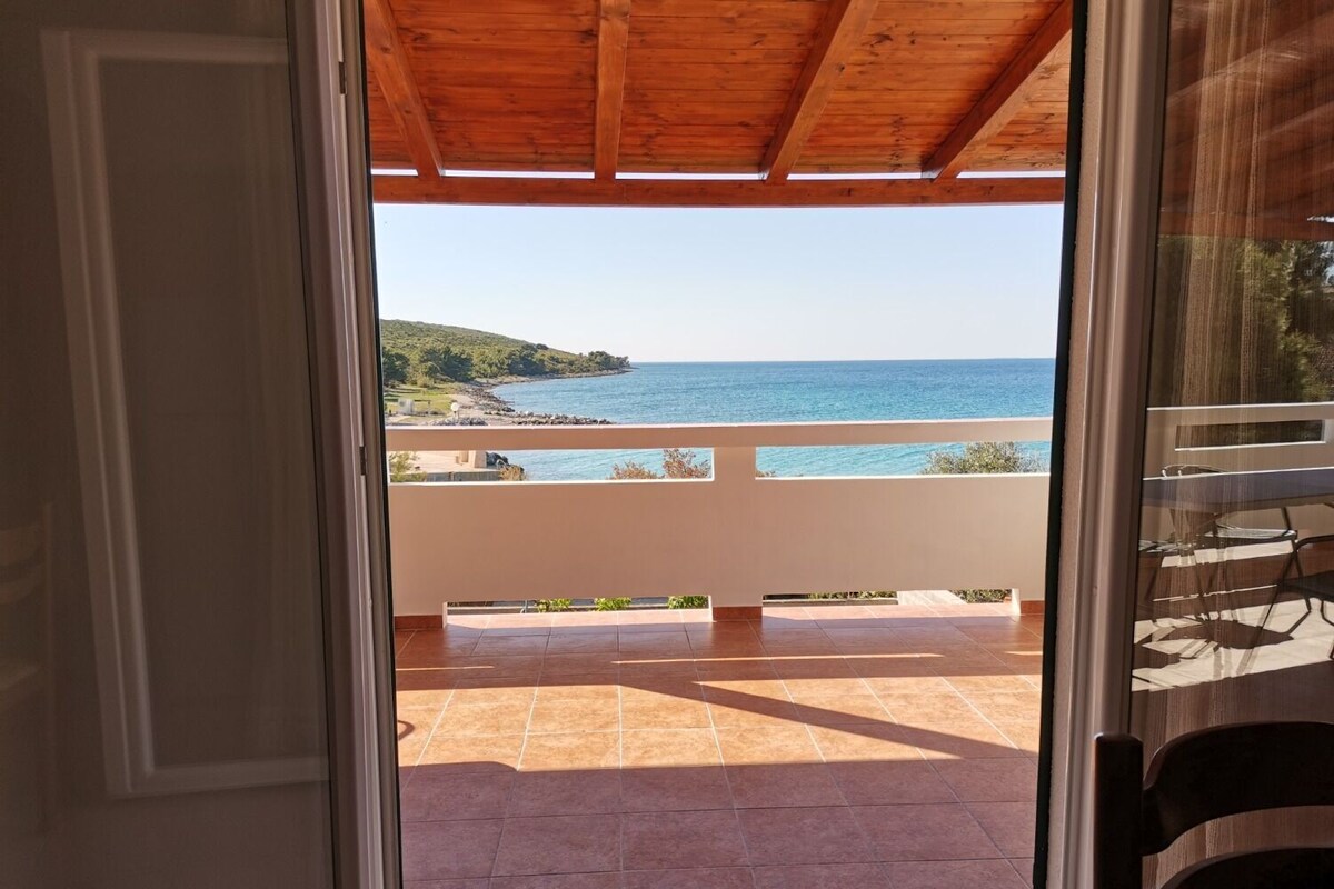 A balcony with a view of the sea and a hilly landscape.