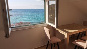 Quarto com uma grande janela com vista para o mar, uma mesa de madeira e duas cadeiras.