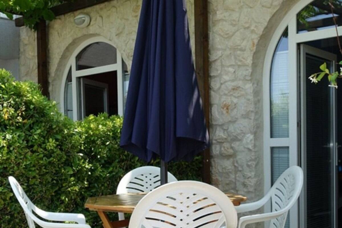 A patio with a stone floor, white plastic chairs, and a table with a blue umbrella.