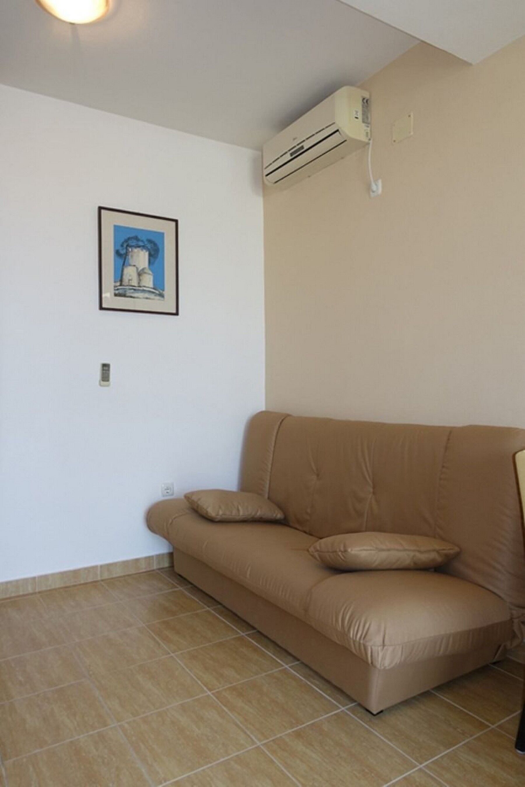 A beige sofa with two cushions in a room with white walls and a tiled floor.