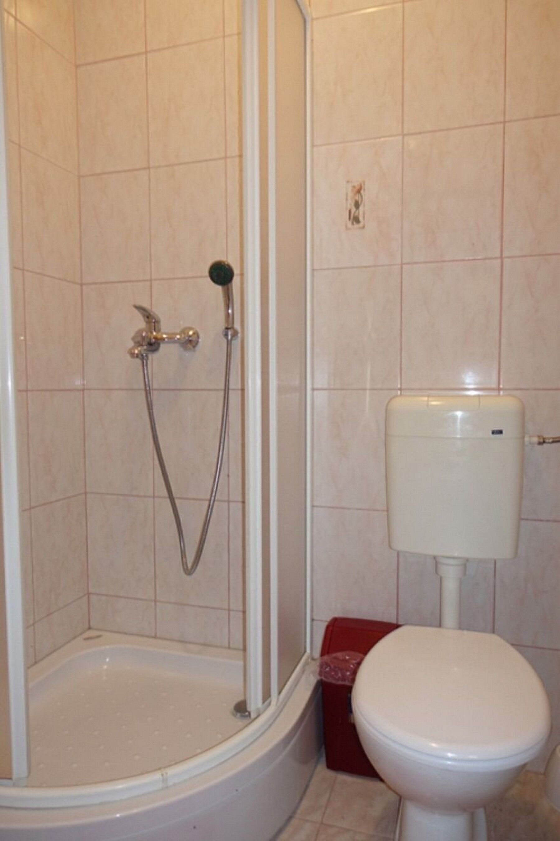 Kylpyhuone, jossa on suihku, wc ja punainen laatikko lattialla.