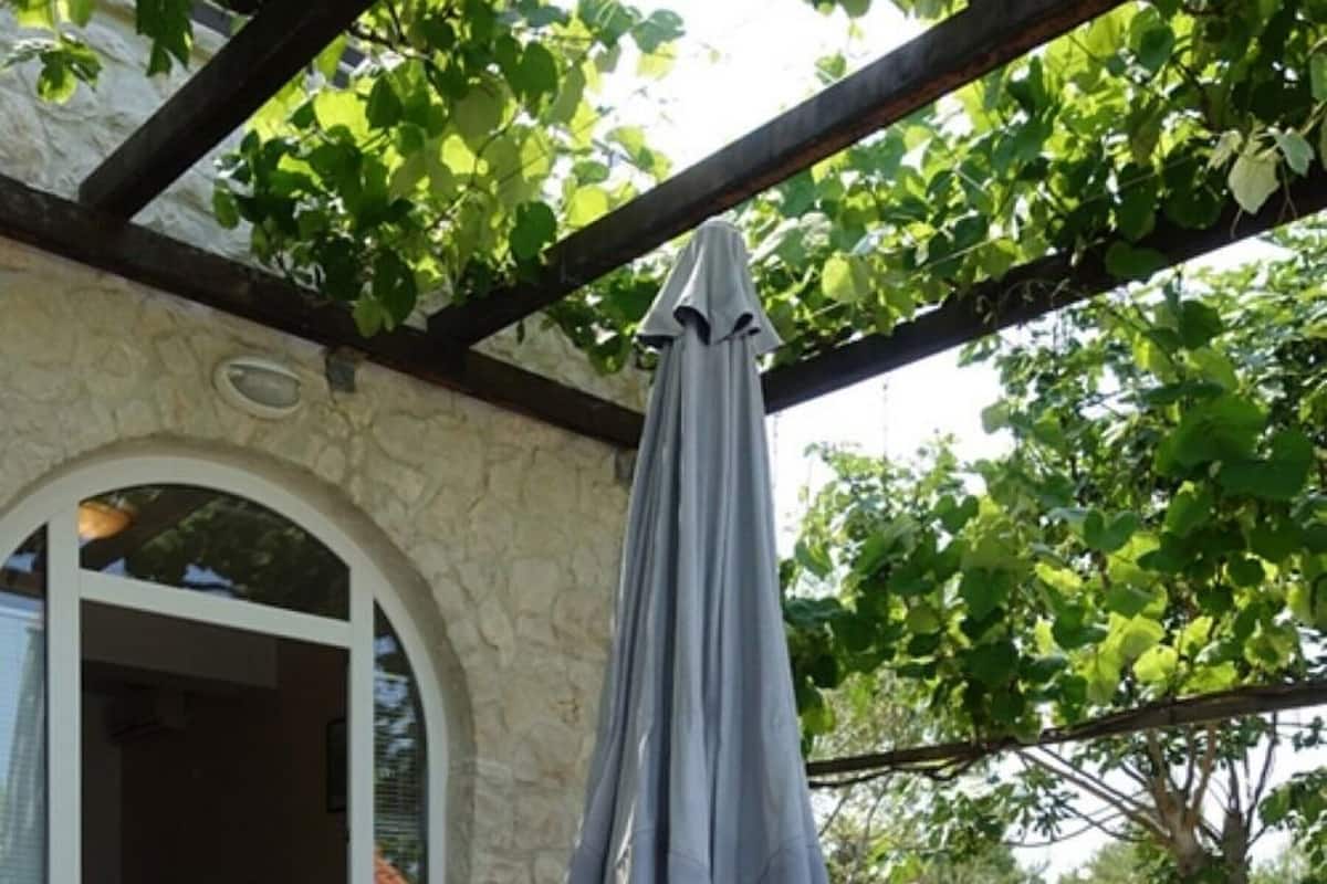 An outdoor patio with a stone floor, white plastic chairs, a wooden table, and a grey umbrella.