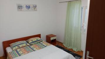 Un dormitorio con cama, mesita de noche, puerta y ventana con cortinas.