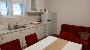 A compact kitchen with white cabinets, a sink, and a refrigerator. There is a dining table with chairs and a red sofa in the living area. - Apartment Bila (Tisno)