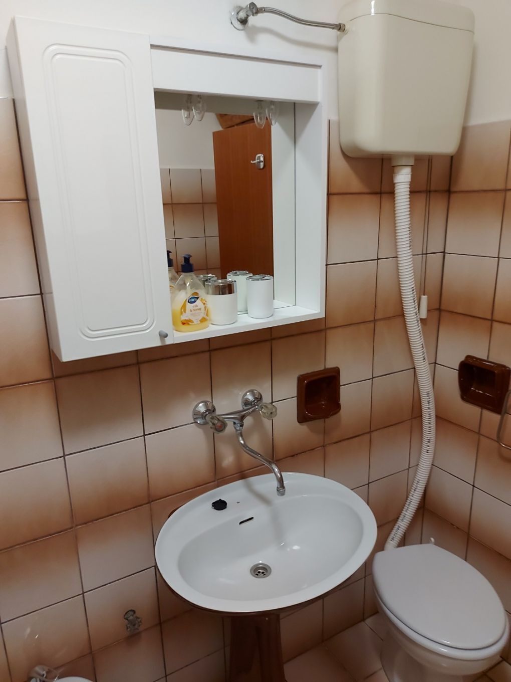 Un baño con lavamanos blanco, inodoro y espejo sobre el lavamanos.