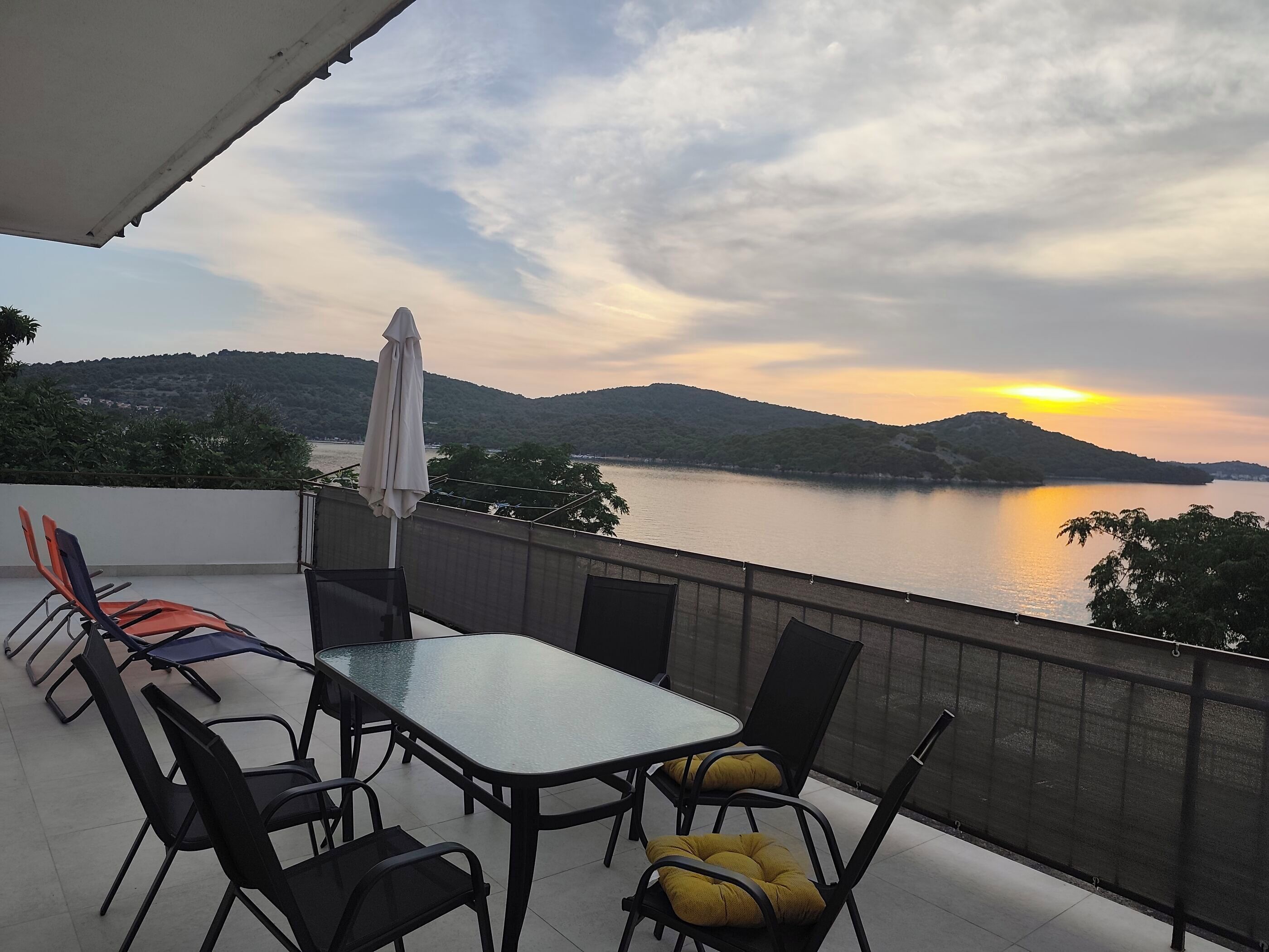 Una terraza con mesa y sillas, con vistas a un cuerpo de agua y colinas.