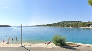 A calm lake with a clear sky, a small island in the distance, and a few people in the water. - Apartment Bila (Tisno)